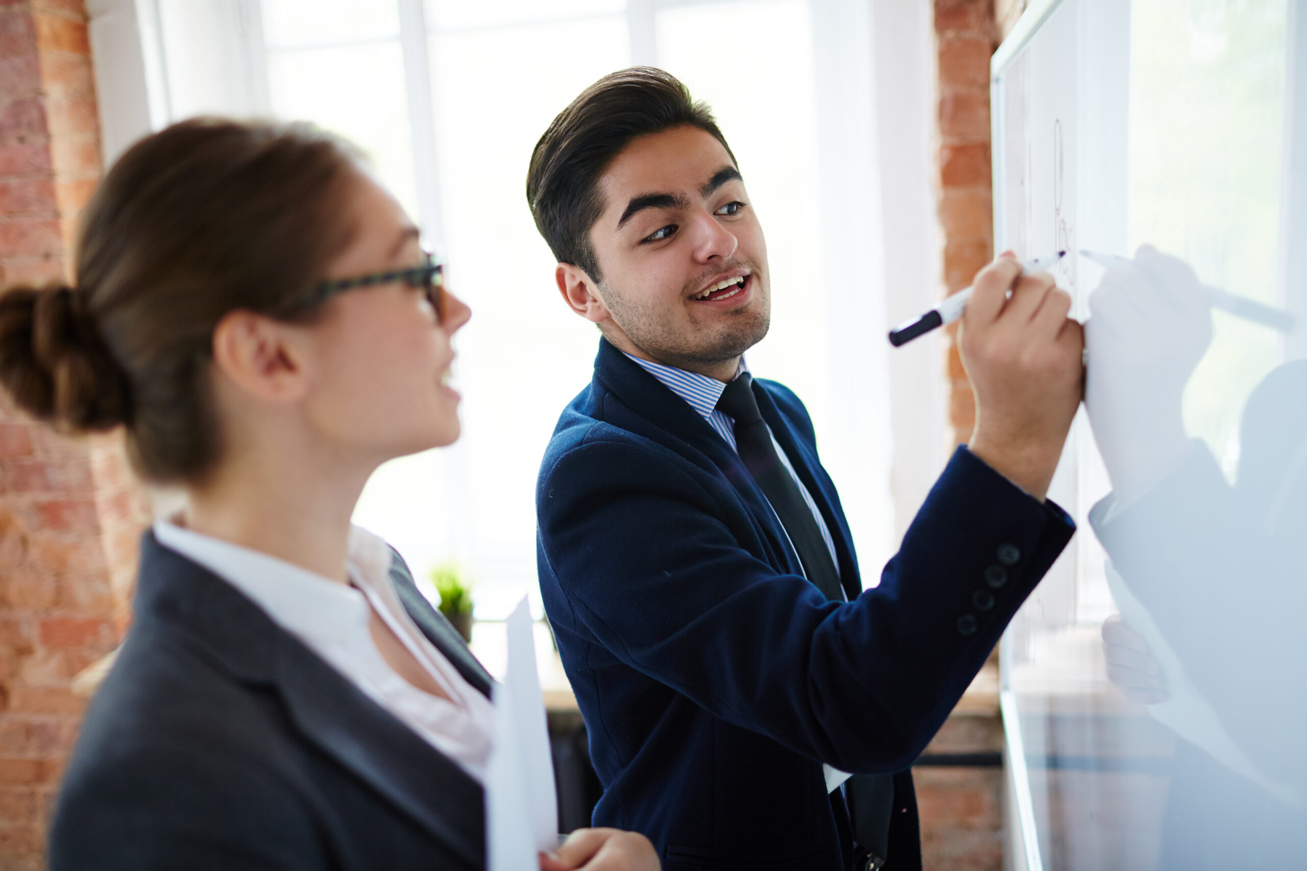 Professional financier analyzing his ideas on whiteboard and explaining them to colleague